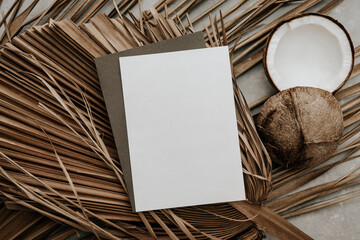 Summer stationery still life with blank paper card , fresh coconut and dry palm leaves on stone...