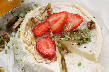 Camembert with strawberries, nuts and honey on a white plate