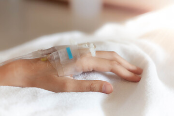 Closeup woman Hand of a patient with medical drip or IV drip lying on bed in hospital, Patient with drip receiving a saline solution. free space for text