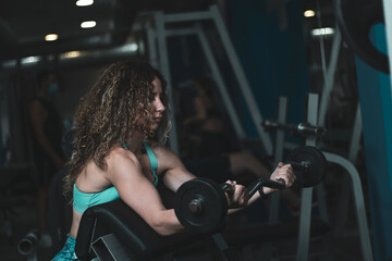 Plakat a young girl with curly hair training with weights inside a gym