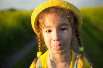 A cheerful girl in a yellow hat in a summer field hooligan shows the tongue and teases....