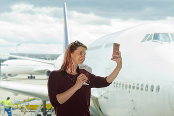 Young female traveler, Blogger in airport lounge near windows with plane happy smile taking selfie photo before flight. Happy girl tourist holding cellphone using camera app making self portrait with