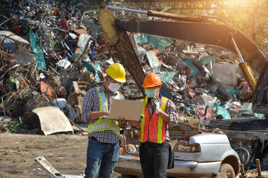 Two workers looking at a laptop at a scrap metal yard, Thailand