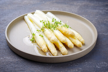 Modern style traditional steamed white asparagus with butter sauce hollandaise and cress served as close-up on a Nordic design plate