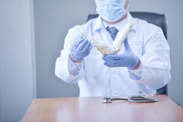 Doctor wearing a face mask holding a artificial foot bone
