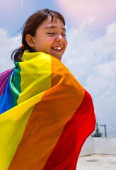 Vertical shot of a small smiling girl with a rainbow flag