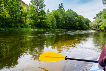 A paddle for rowing yellow in the hands of a girl while kayaking on the river