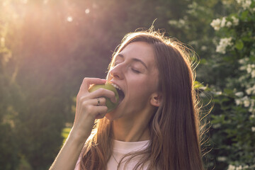 Young woman biting green apple outdoors. Healthy eating.