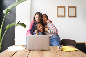 A group of women hugging each other euphorically celebrate the good news in front of the computer....