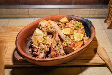 Homemade grilled chicken with spices cut into pieces in red ceramic baking dish on wooden board.