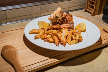 Homemade grilled chicken served on a ceramic white plate with with rustic fried potatoes and sauce. Isolated over wooden board.