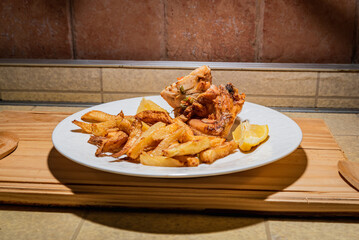 Homemade grilled chicken served on a ceramic white plate with with rustic fried potatoes and sauce. Isolated over wooden board.