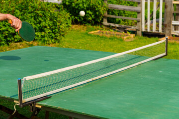 Hand with a racket, playing table tennis outdoors in the yard, hits the ball