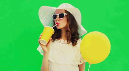 Portrait of beautiful young woman drinking juice wearing a white summer straw hat on green background