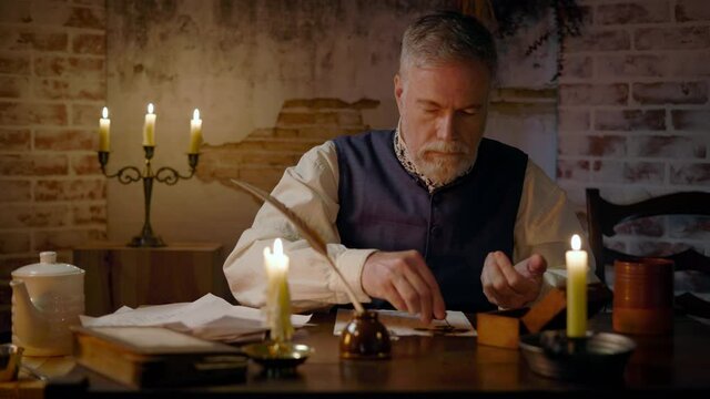 A cozy 18th century scene lit by firelight and candlelight of a gentleman making an accounting of his coin collection.