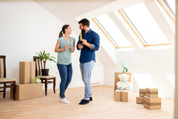 Fototapeta na wymiar Young caucasian couple opening champagne bottle to celebrate moving into new apartment.
