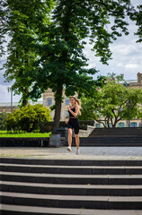 A young blonde woman with a sporty physique in a black T-shirt and in black tight sports shorts runs up the stairs