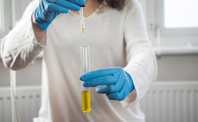 Clean and sterile gloved person dropping solution with a dropper pipette in a test tube
