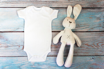 White baby bodysuit mockup with toy on wooden background. Styled stock photography. Mock up