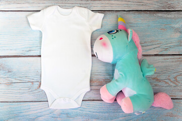 White baby bodysuit mockup with unicorn toy on wooden background. Styled stock photography. Mock up