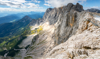 View of Hoher Dachstein from Skywalk, or Honerkogel, on a sunny summer day. Tall, rocky Alpine peaks and vast valley below from a viewpoint nearby.