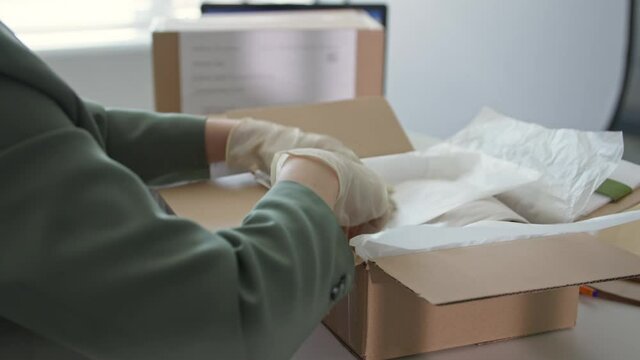 small business in quarantine, young female salesman in medical gloves packing goods in box for delivery to customers of an intranet clothing store, close-up