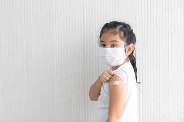 Asian cute girl wearing face mask showing vaccinated arm. Covid-19 Vaccination concept.
