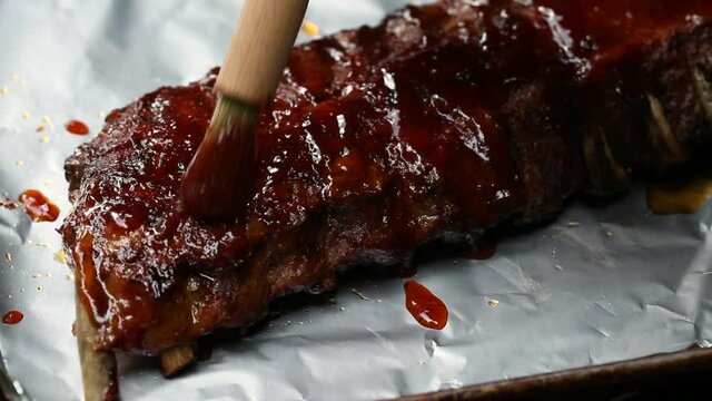 Brushing BBQ sauce on grilled rack of ribs on foil