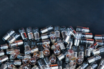 Many small incandescent bulbs lie in a heap on a black background, close-up.