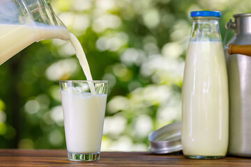 milk pouring from jug into glass outdoors - obrazy, fototapety, plakaty