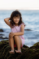 Young girl sitting on the rock near the ocean. Smiling girl. Happy childhood. Spending time on the beach. Vacation in Asia. Pandawa beach, Bali, Indonesia