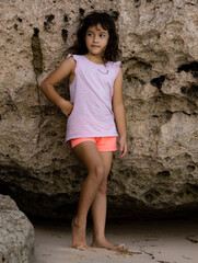 Young girl standing near the rock. Happy childhood. Spending time on the beach. Girl wearing shorts. Vacation in Asia. Pandawa beach, Bali, Indonesia