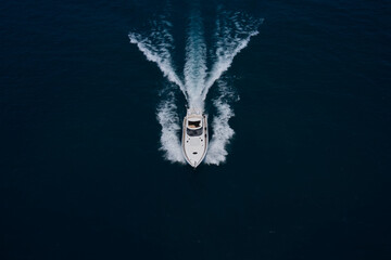 Large white yacht on the water in motion top view. Luxury motor boat on dark blue water aerial view. The yacht is fast moving on dark water. Travel on high-speed boats on the water.