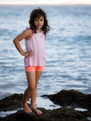 Fototapeta na wymiar Young girl standing on the rock near the ocean enjoying nature. Happy childhood. Spending time on the beach. Vacation in Asia. Pandawa beach, Bali, Indonesia