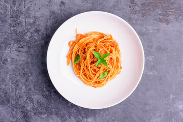 Freshly cooked classic Italian spaghetti pasta prepared in a white plate, on a dark table - top view.