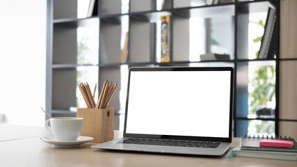 Mock up laptop computer, pencil holder and coffee cup on wooden desk.