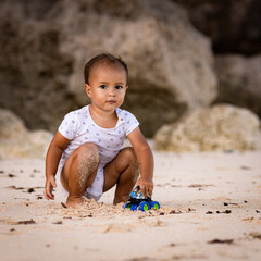 Baby boy sitting on sandy beach, playing with toy car. Warm sunny day. Happy childhood. Summer vacation at the sea. Spending time near the ocean. Pandawa beach, Bali, Indonesia