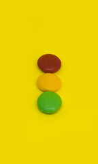 Obraz na płótnie Canvas Colored chocolate lentils forming a traffic light on an absolute yellow background. Colorful Chocolate Candy.