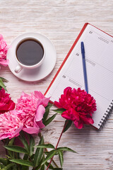 Morning coffee mug for breakfast, empty notebook, pencil and pink peony flowers on white stone table top view in flat lay style.