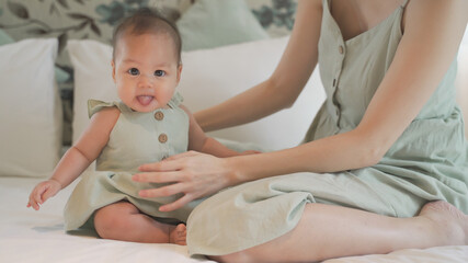 Obraz premium asian woman mother parent encourage baby infant to sit and crawl on soft bed at luxury home. 6 months kid put effort learning lesson development skill. mom playing with baby infant on bed in bedroom.