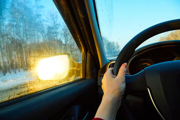 The hand of driver on the steering wheel of the car and the blue sky in the evening outside the windshield
