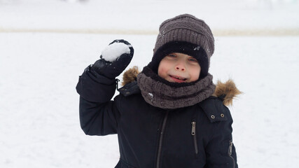 Fototapeta na wymiar A boy in winter clothes aims a lump of snow at a friend in winter on a walk