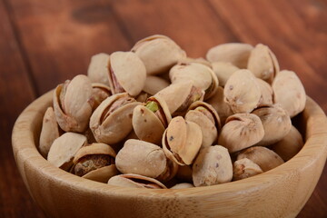 Pistachios in a wooden bowl on wooden surface, pile of pistachios, roasted pistachios in a bowl