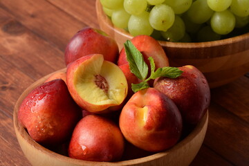 Fototapeta na wymiar Nectarine and Bunch of green ripe grapes in a wooden bowls on a table. Rustic style