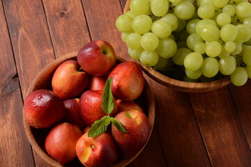 Nectarine and Bunch of green ripe grapes in a wooden bowls on a table. Rustic style
