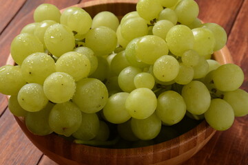 Bunch of green grapes in a wooden bowl, fruits of autumn, on rustic wooden background