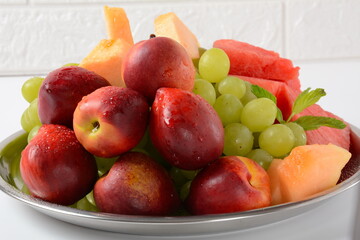 Naklejka na ściany i meble Fruit mix. Nectarine, grapes, watermelon, melon. Pieces of fruit on a plate lie on a silver tray on white background.
