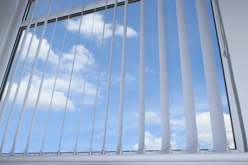 Vertical white window blinds in a domestic situation with a bright blue sky background - UK