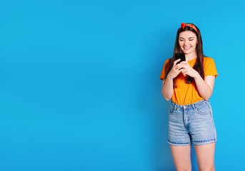 A fashionable pretty cute carefree woman browsing a smartphone, dressed in a colorful orange bandana. the concept of summer