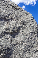 A fragment of a rock on the background of a blue sky with clouds. The relief and pattern of the rock. Natural background and stone texture.